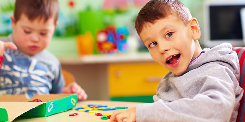 An image of two young children seated together at a table in a classroom environment interacting with coloured shapes.