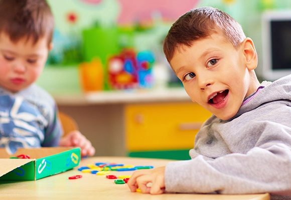 An image of two young children seated together at a table in a classroom environment interacting with coloured shapes.